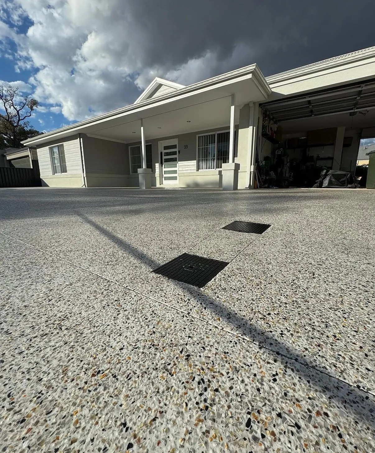 Wide exposed aggregate driveway running up to the garage of a single storey suburban home under a cloudy sky