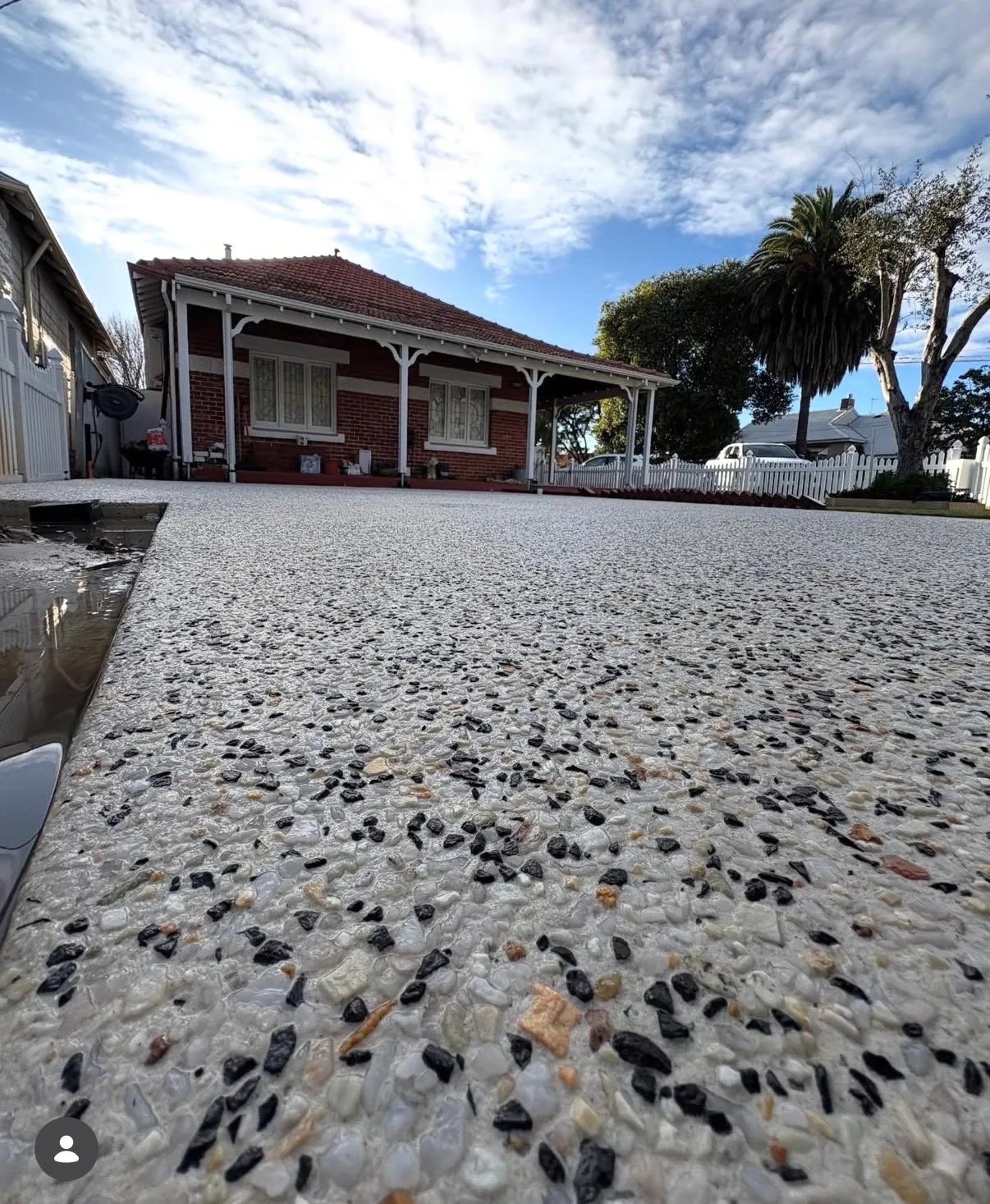 Ground-level view of a white and black pebble exposed aggregate driveway running up to the verandah of a red brick home