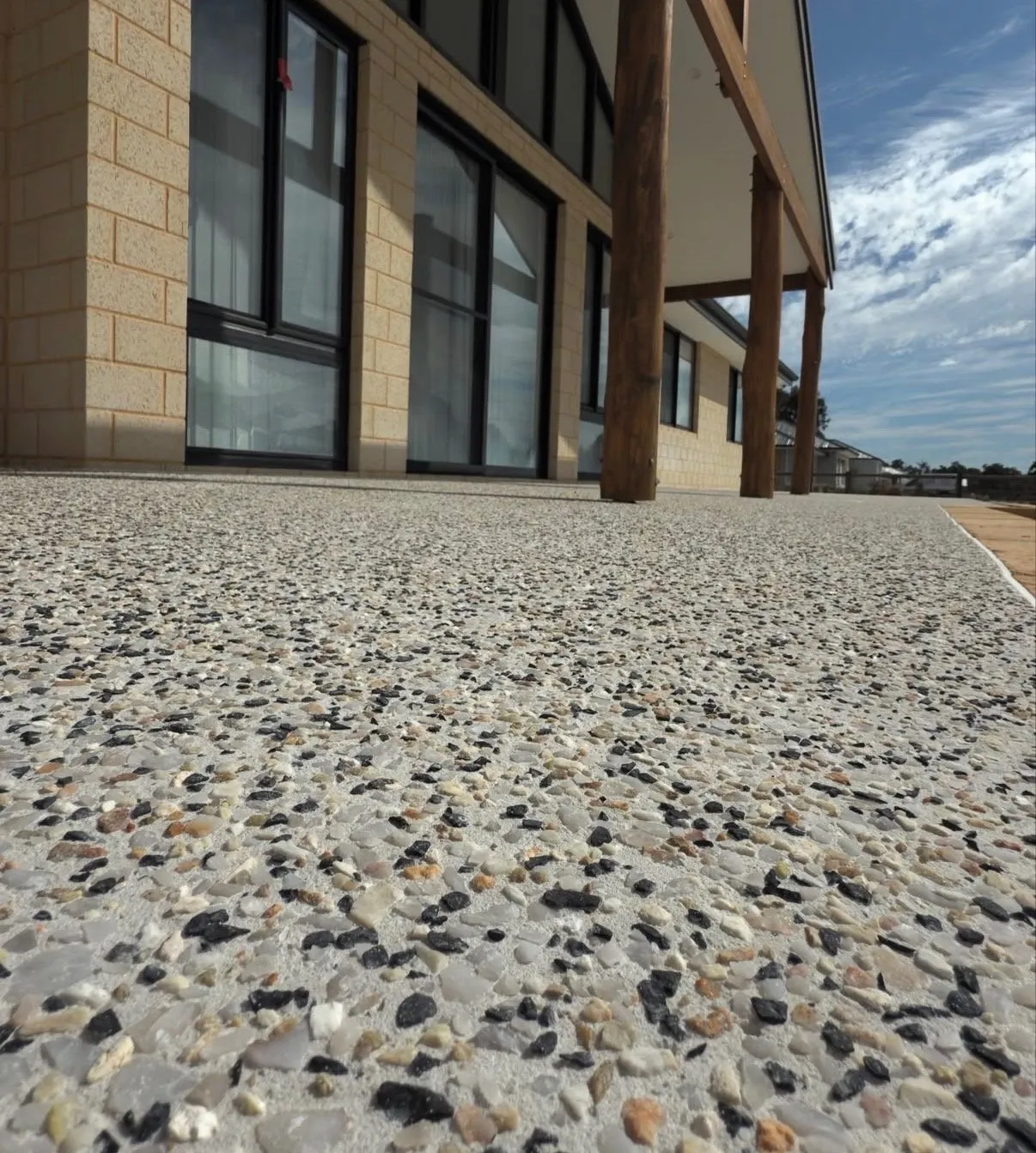 Honey and charcoal exposed aggregate paving running along a limestone-block home with timber verandah posts