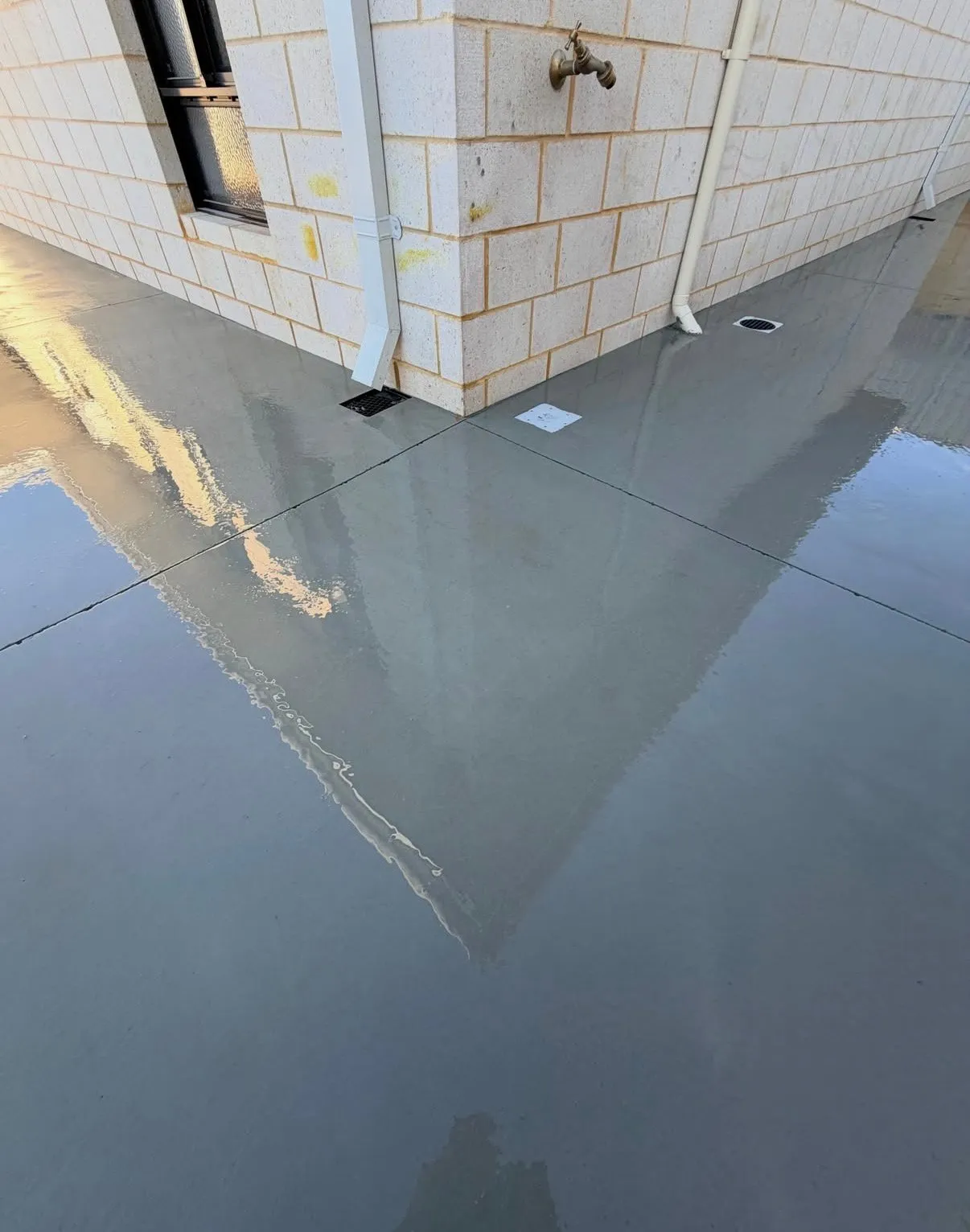 Freshly sealed honed concrete alongside a cream brick wall, the wet surface reflecting the building back