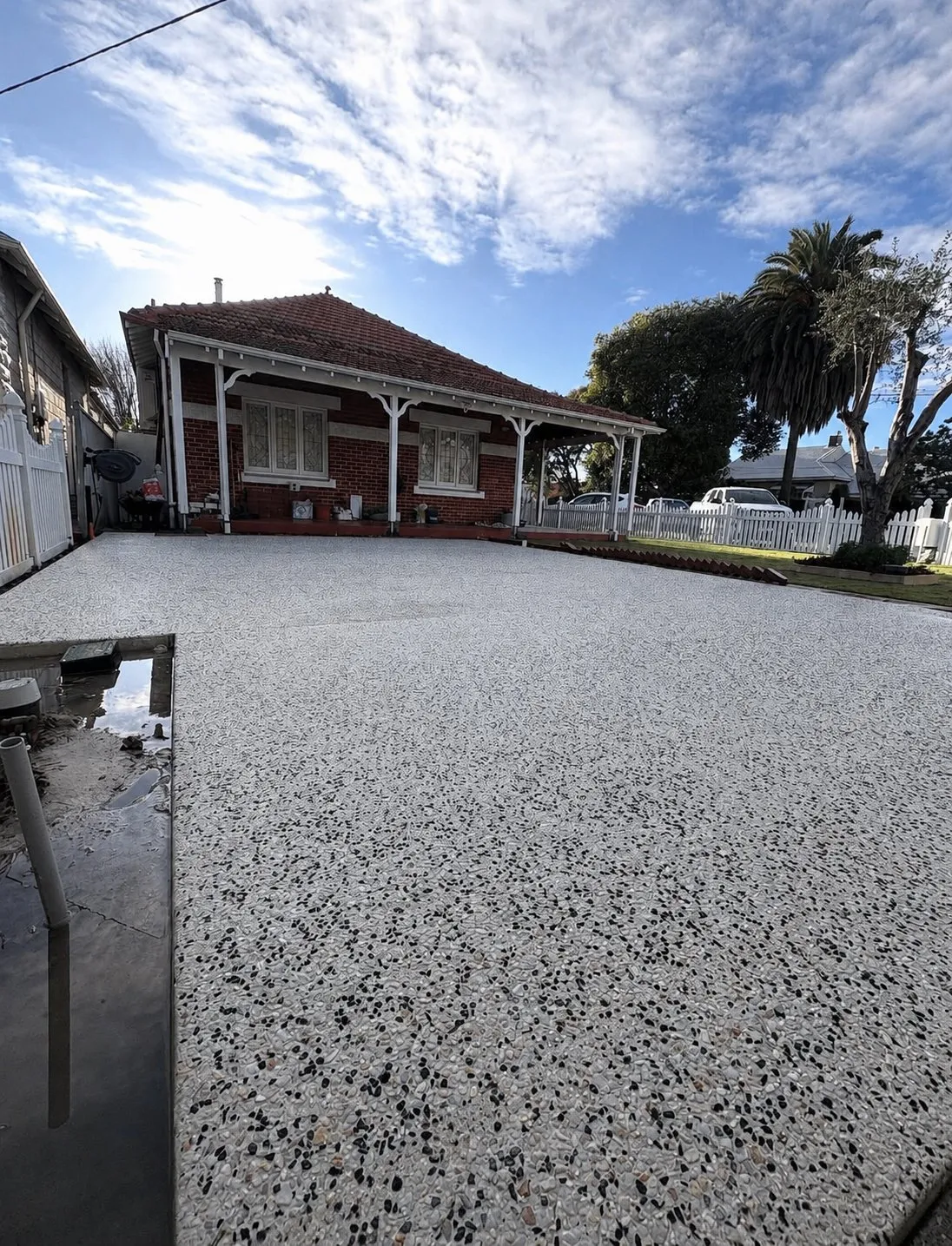 Wide white and black pebble exposed aggregate driveway covering the full frontage of a red brick home with a white verandah
