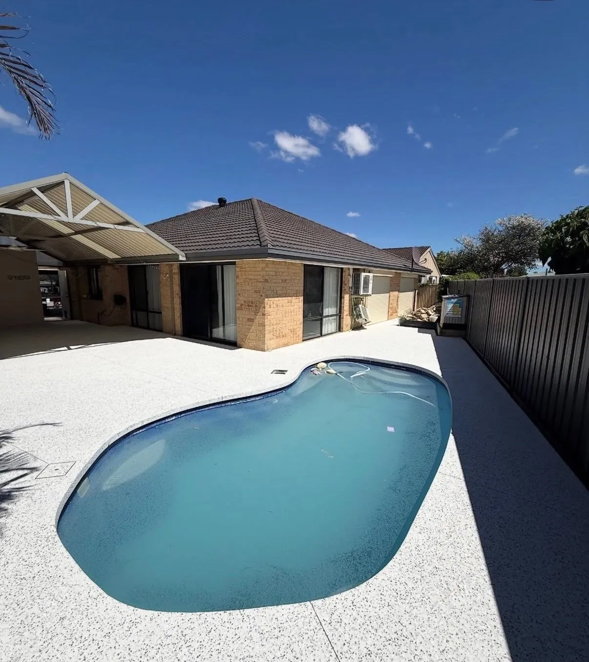 White exposed aggregate pool surround laid around a kidney-shaped pool at a cream brick home