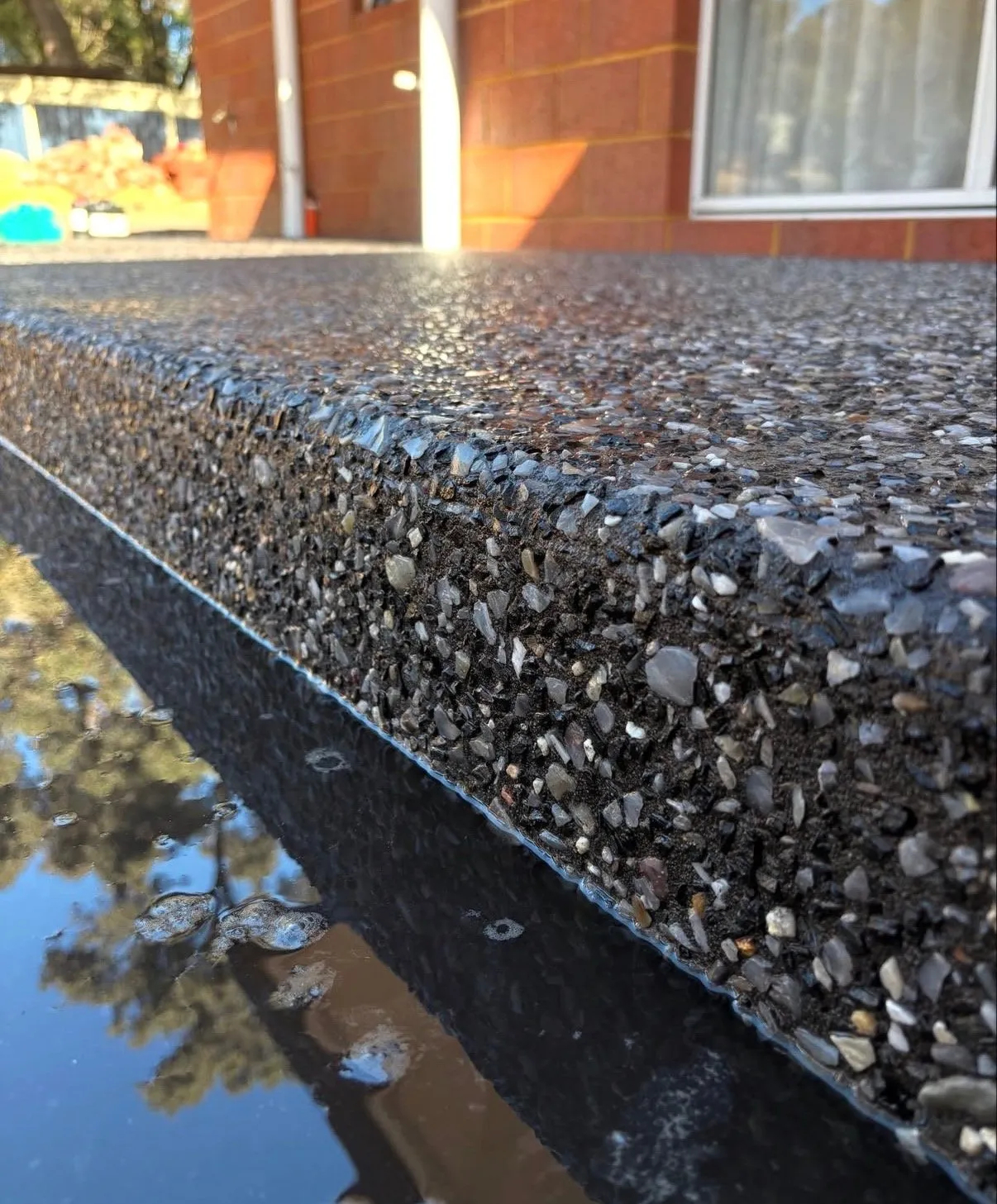 Close-up of a dark exposed aggregate step with a crisp cast edge, the stones washed clean and still wet after rain