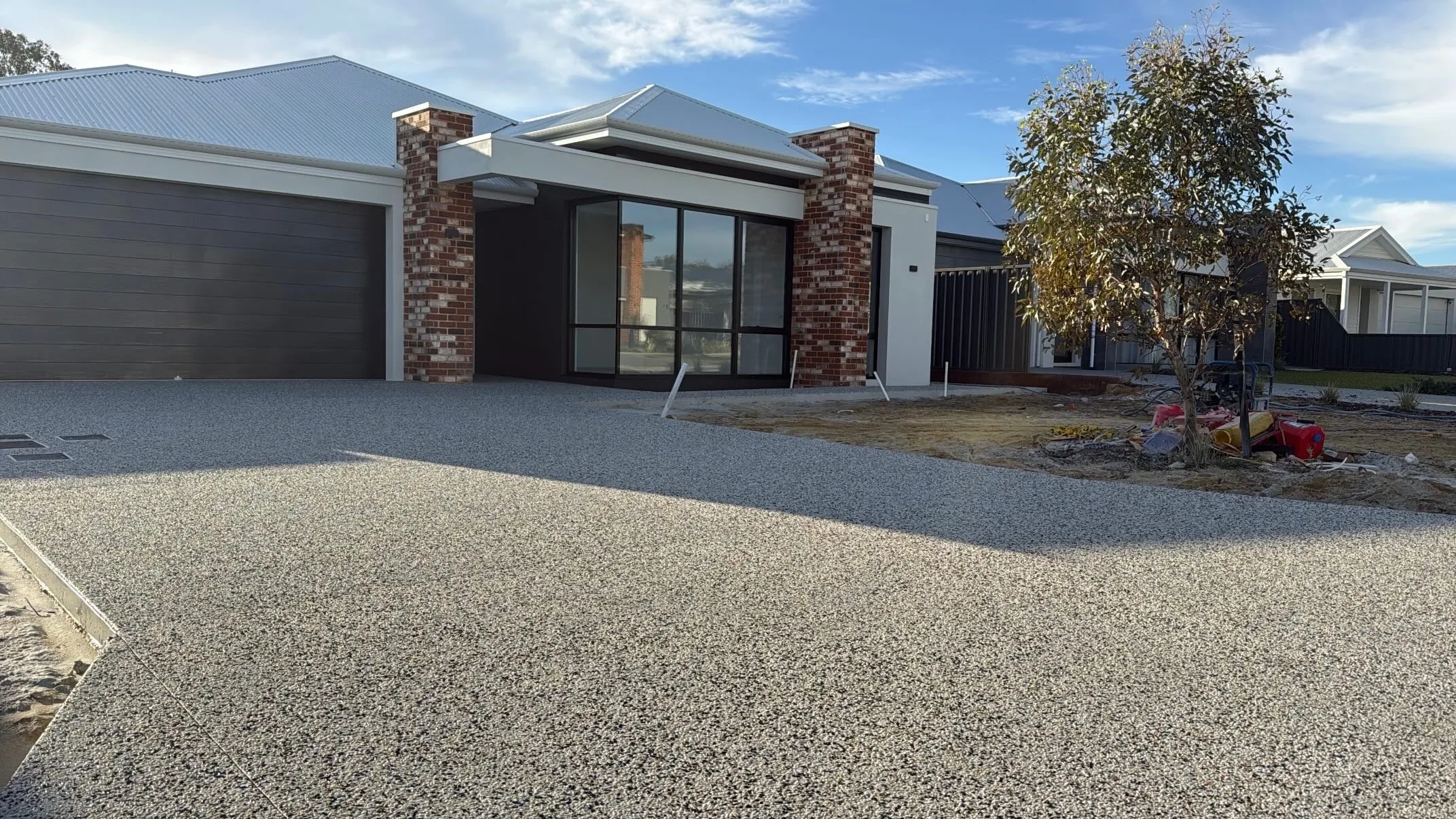 Wide pale grey exposed aggregate driveway running to a double garage at a newly built home with red brick piers