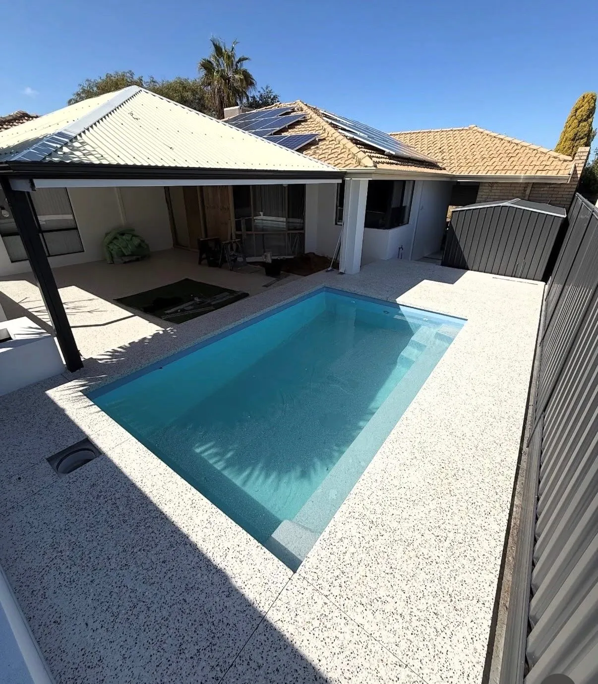 White and black exposed aggregate pool surround around a rectangular pool, running up to a covered alfresco area