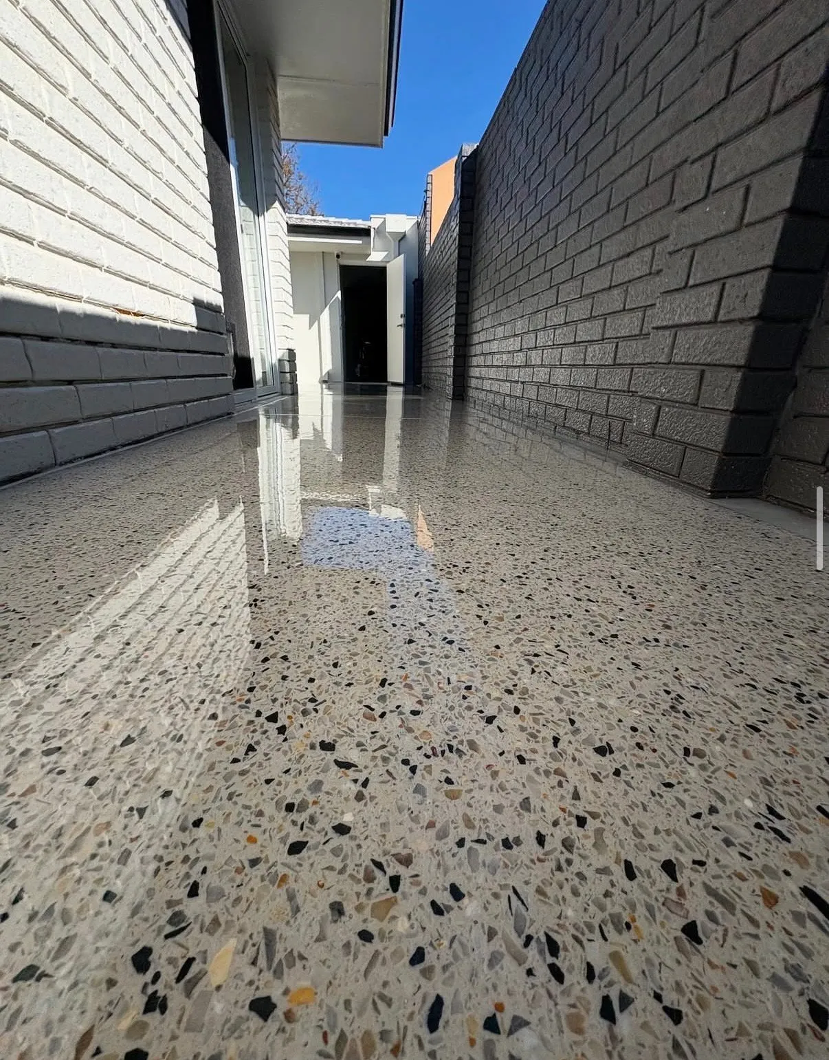 Honed exposed aggregate path with a high polish and heavy black and grey stone reveal, running between a white brick wall and a charcoal brick wall