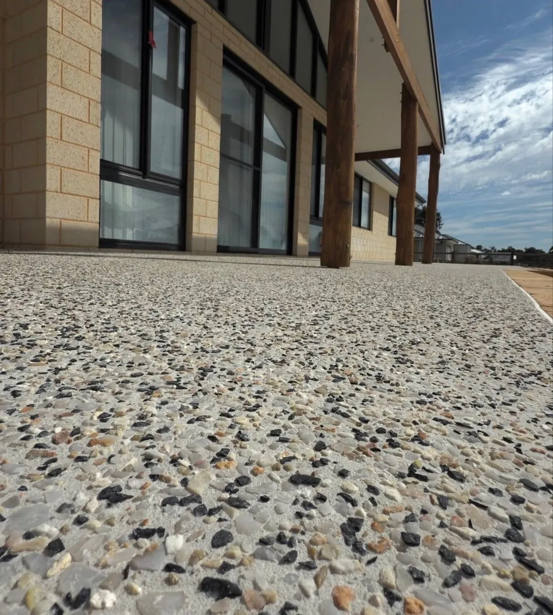 Exposed aggregate paving running up to a rendered home with timber posts, the washed stone surface filling the foreground