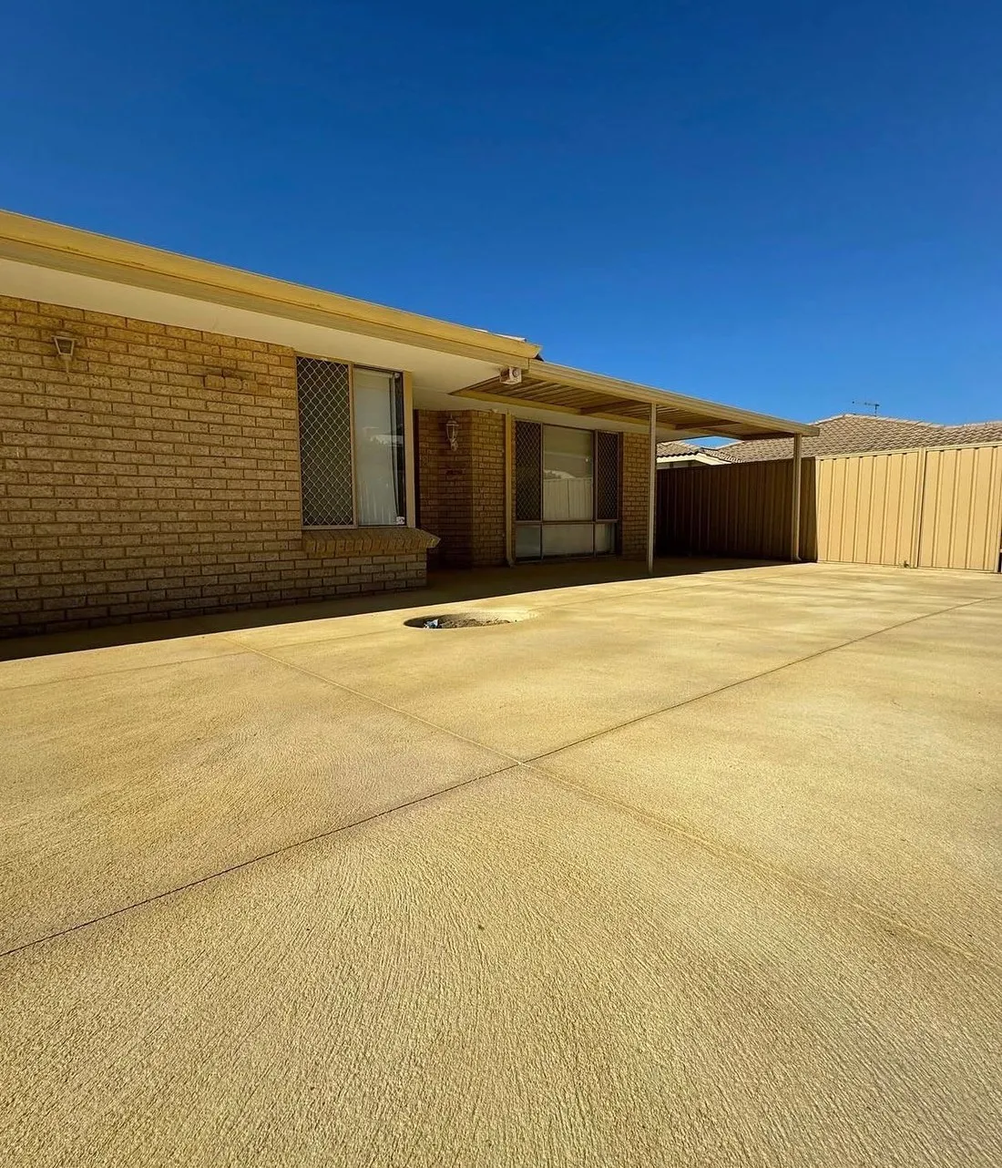 Warm sand-coloured liquid limestone laid across a backyard and continuing under the patio roof of a cream brick home