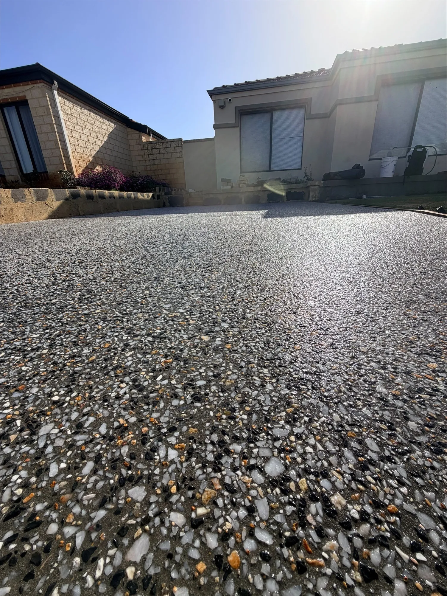 The Canning Vale driveway looking towards the house, dark exposed aggregate meeting a limestone block garden wall and a cream rendered home in low sun