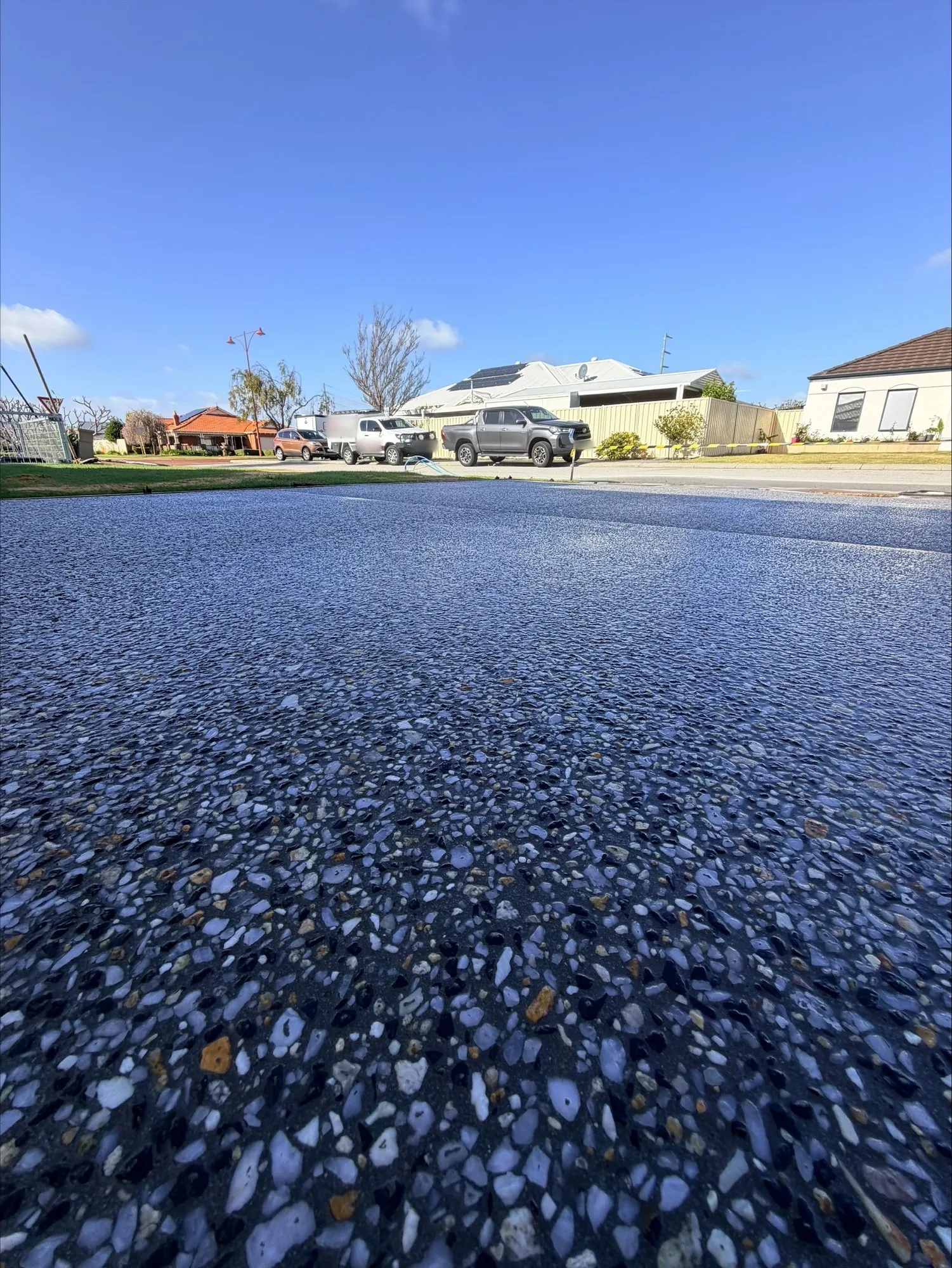 Kajaani Grey exposed aggregate driveway in Canning Vale shot from ground level, charcoal concrete with white, grey and amber stone running out to the street