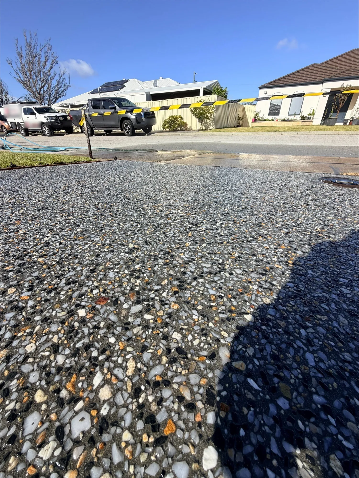 Close-up of the Kajaani Grey exposed aggregate at the street end of the Canning Vale driveway, still taped off, with the road and parked utes behind