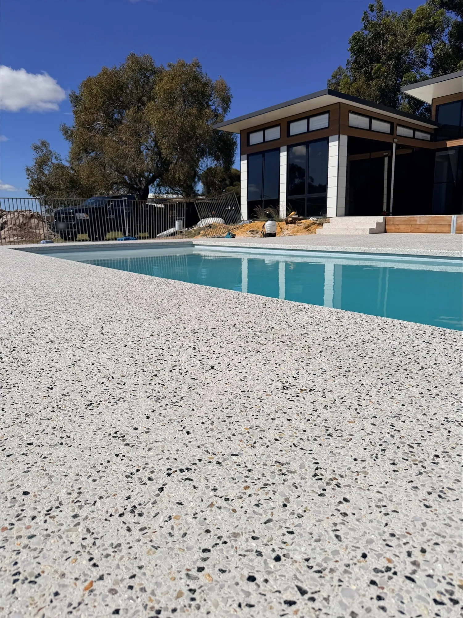 Low close-up of the white exposed aggregate pool surround in North Dandalup, showing cream, black and amber stones, with the pool and house behind