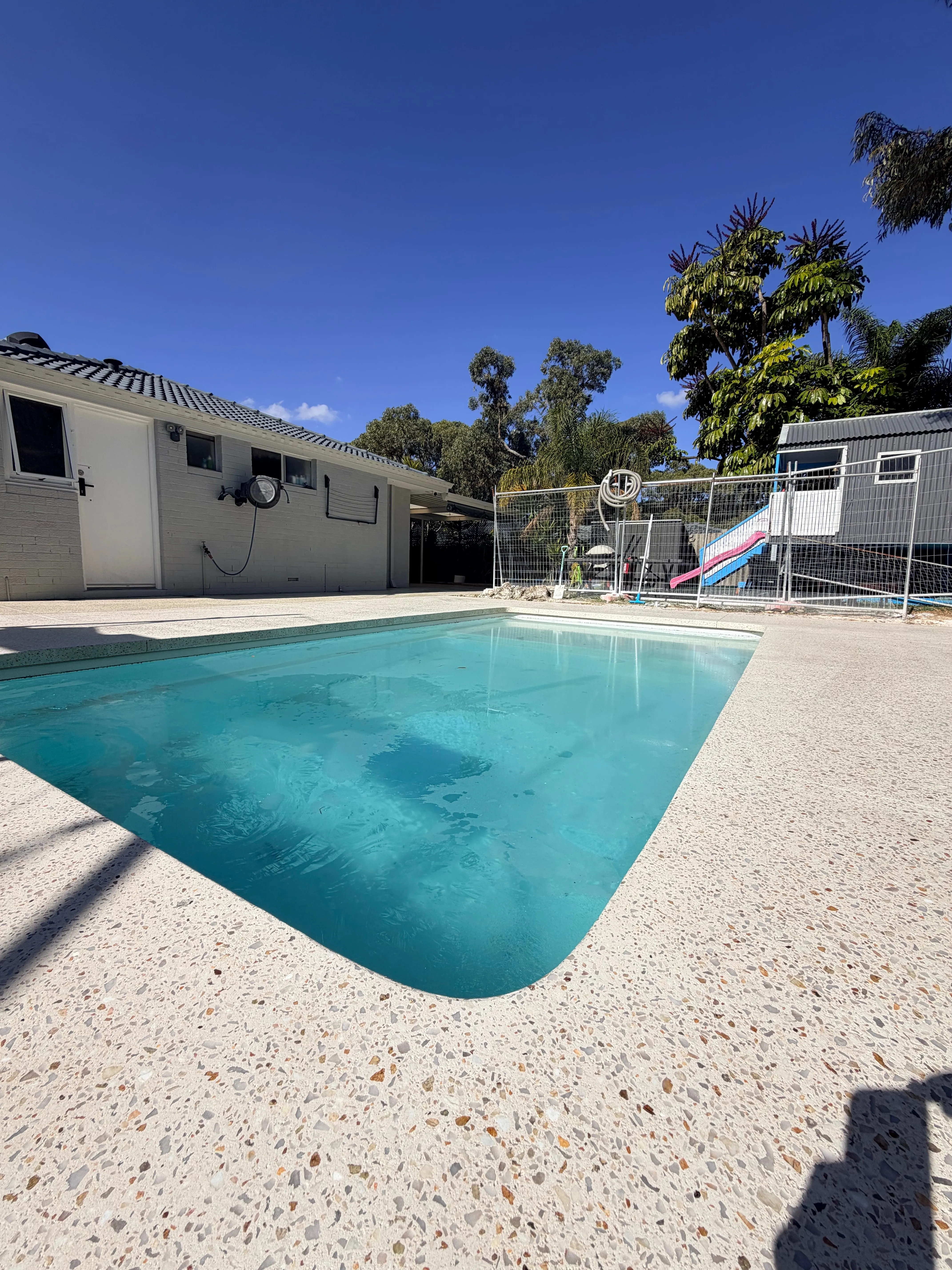 Cream exposed aggregate pool surround wrapping a rectangular pool in a large open backyard